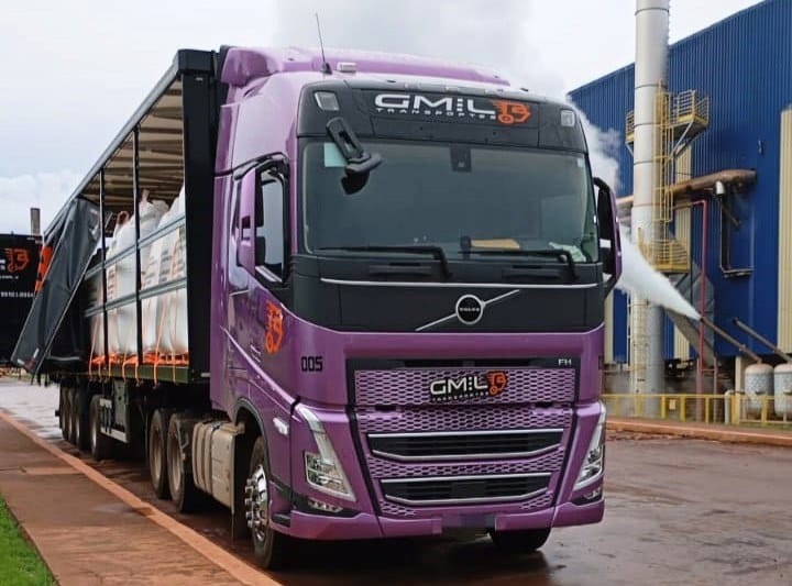 Cavalo roxo da GMIL carregando carreta sider aberta na frente de uma indústria